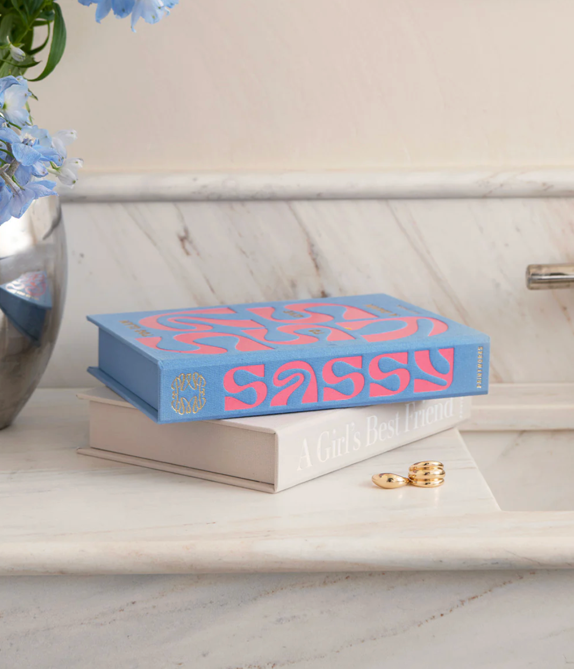 Blue and pink jewelry box on marble counter with gold ring stack