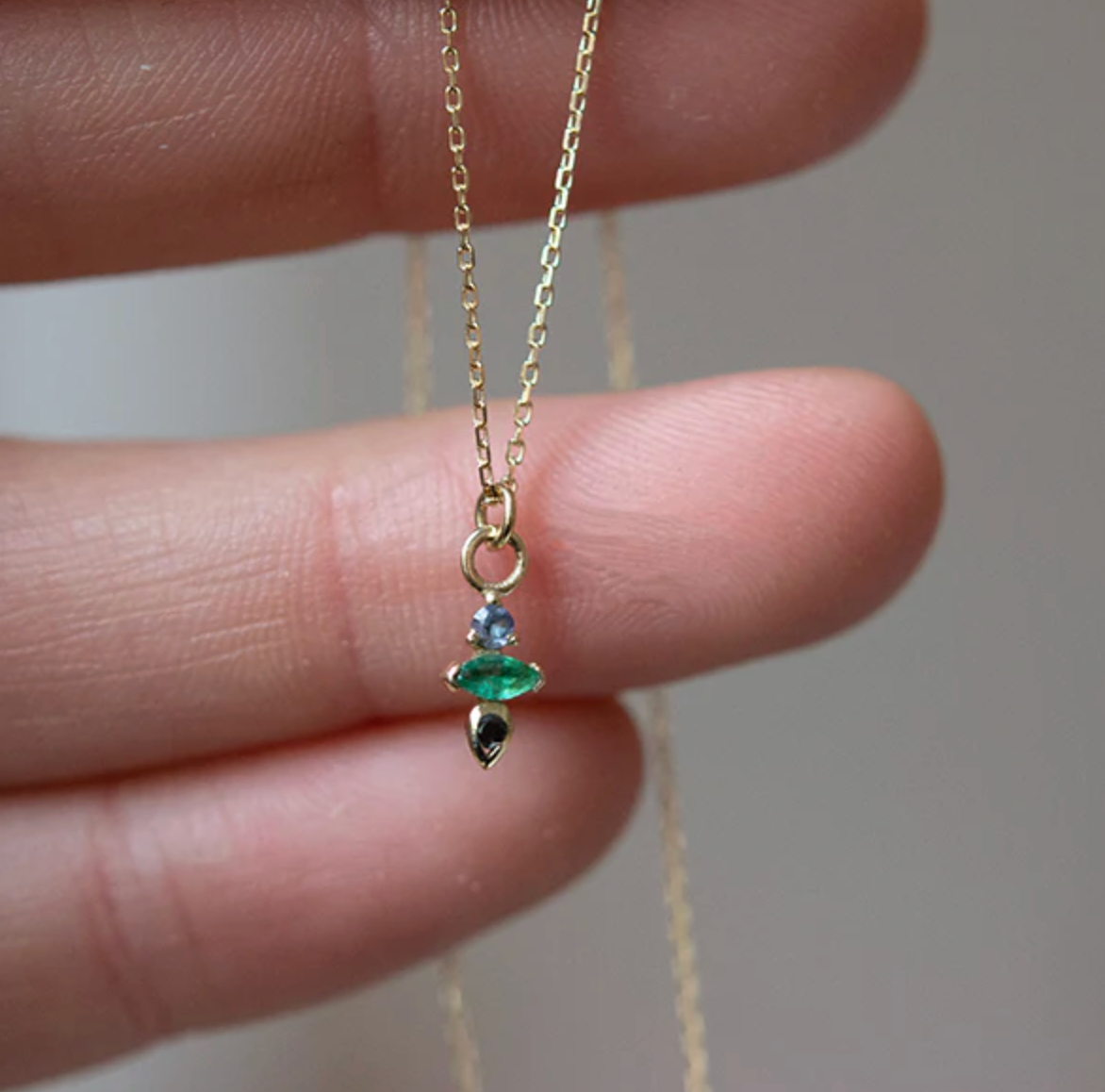 hand holding the gold necklace with emerald, tanzanite and black diamond pendant