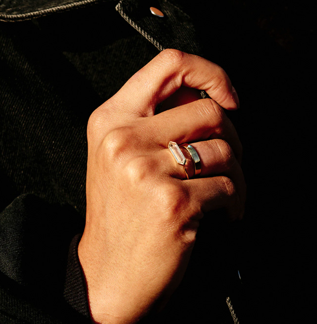hand wearing a hexagon gemstone ring stacked with a gold band on black background.