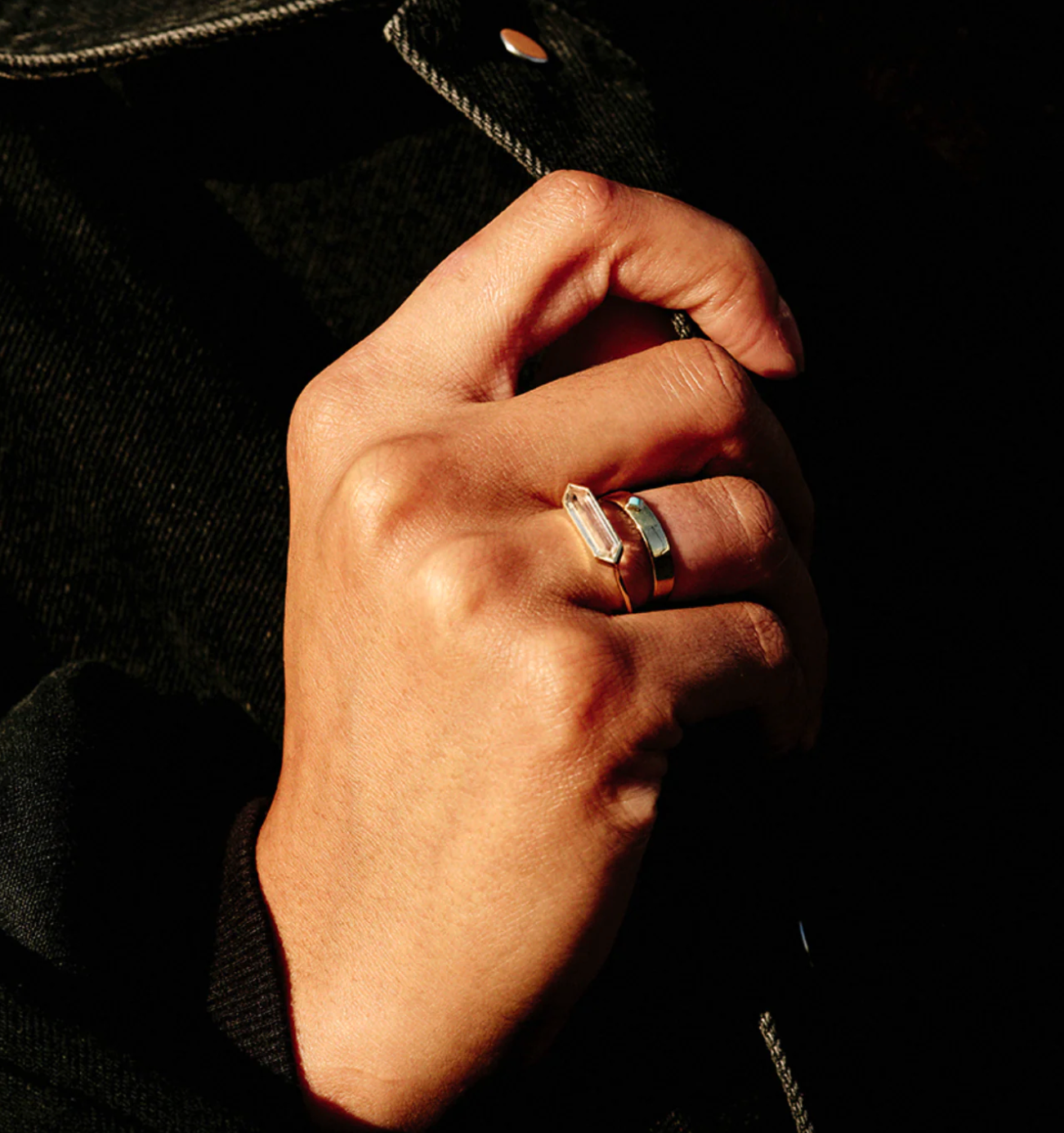 hand wearing hexagon gemstone ring stacked with gold band on black background
