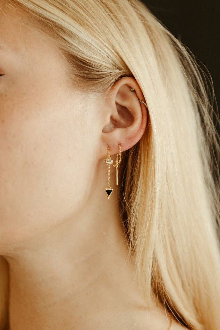 Close-up of a person wearing gold earrings with a black triangle detail.