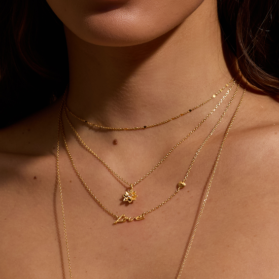 model wearing the love necklace layered with three other dainty gold necklaces