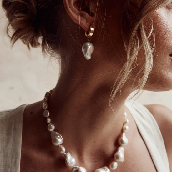 model wearing the gold huggie pearl hoops with a pearl necklace