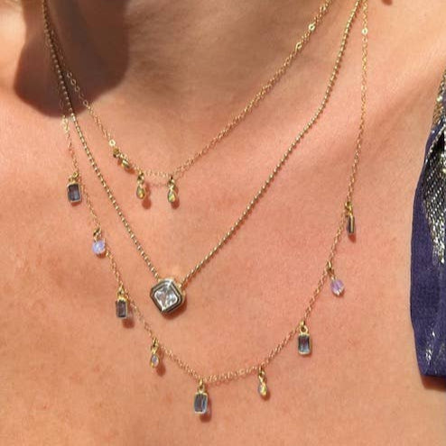 Close-up of a person wearing multiple necklaces and rings with sunlight casting shadows.