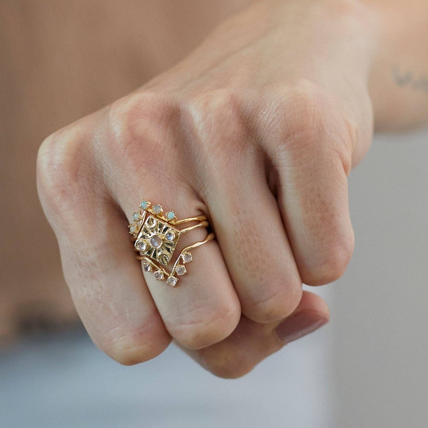 Close-up of a hand wearing a gold ring with gemstones on a neutral background