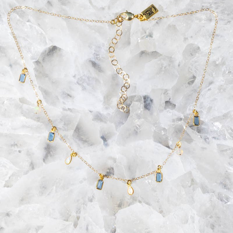 Gold necklace with small colorful stones on a marble surface
