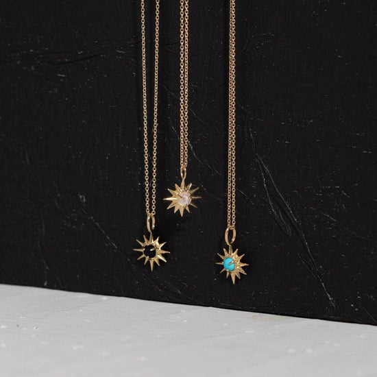 Three gold necklaces with sun-shaped pendants on a black background