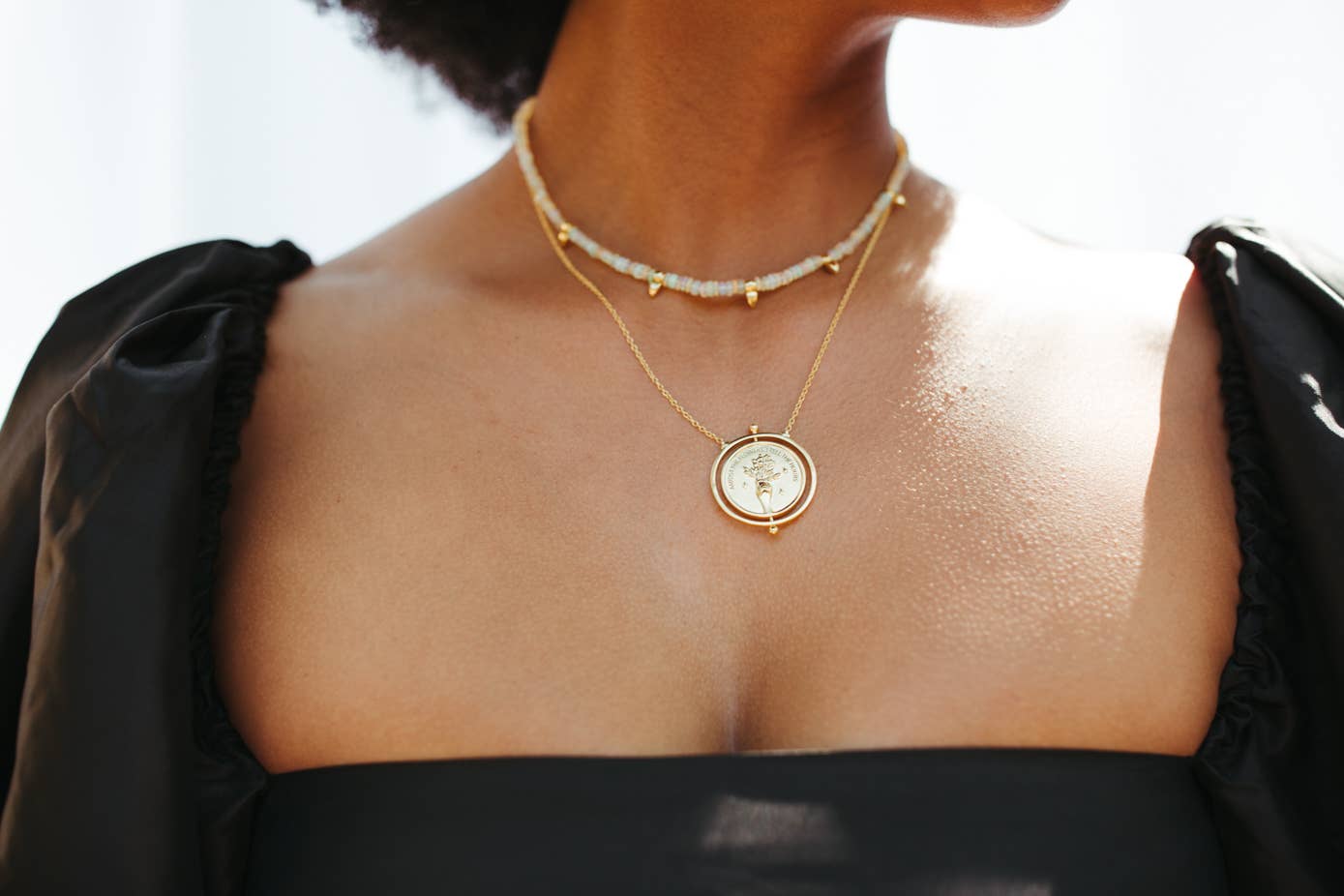 Close-up of a person wearing a gold necklace with a circular pendant.
