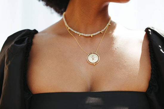 Close-up of a person wearing a gold necklace with a circular pendant.