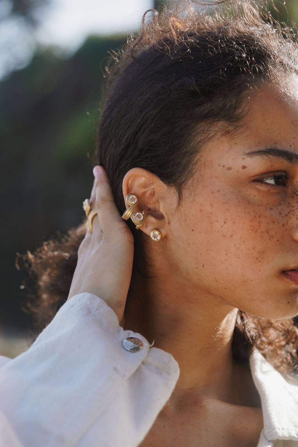 Close-up of a person wearing gold earrings with a blurred natural background