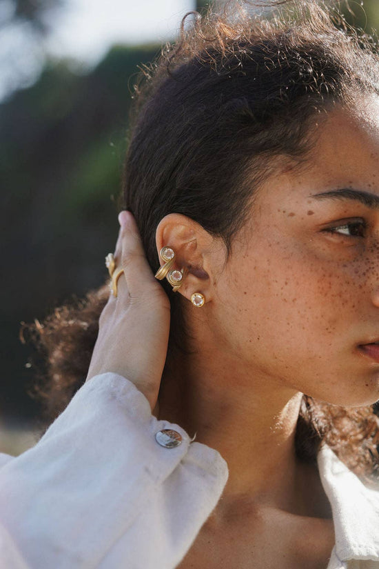 Close-up of a person wearing gold earrings with a blurred natural background