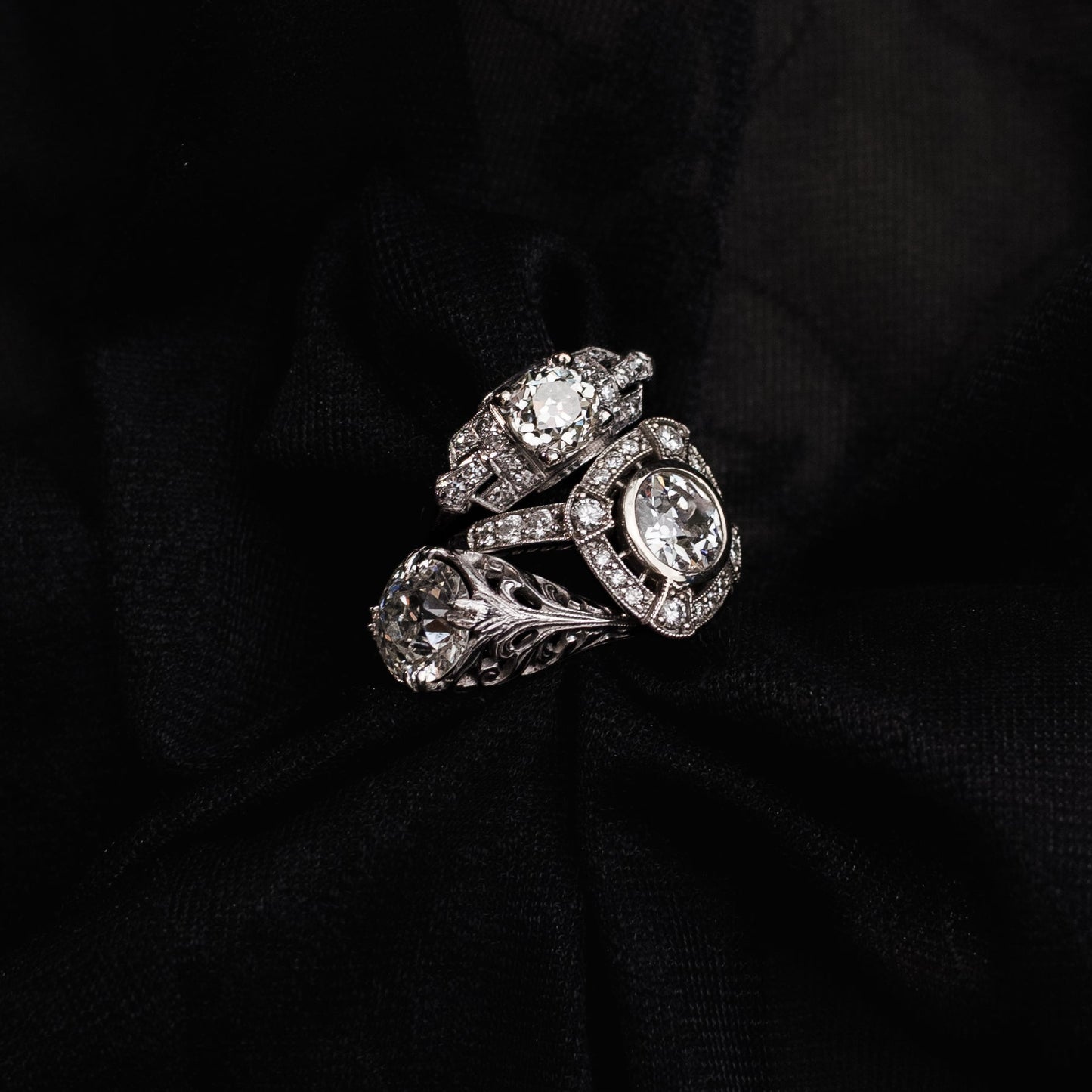 A silver-toned vintage-style ring with multiple round clear gemstones, displayed on a draped black fabric background.