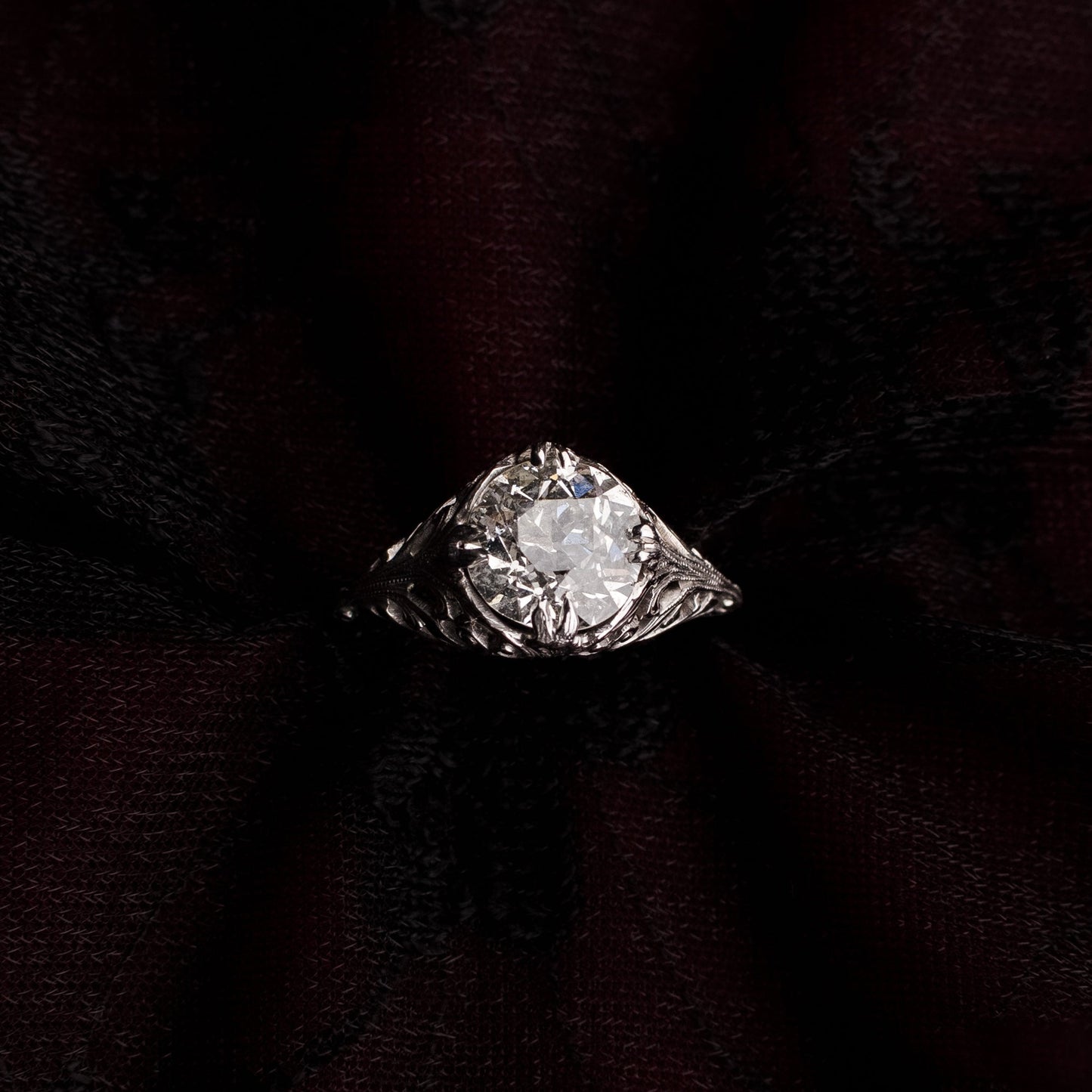 A vintage-style diamond ring with a marquise-cut center stone and silver-toned setting, displayed on a dark burgundy fabric backdrop.