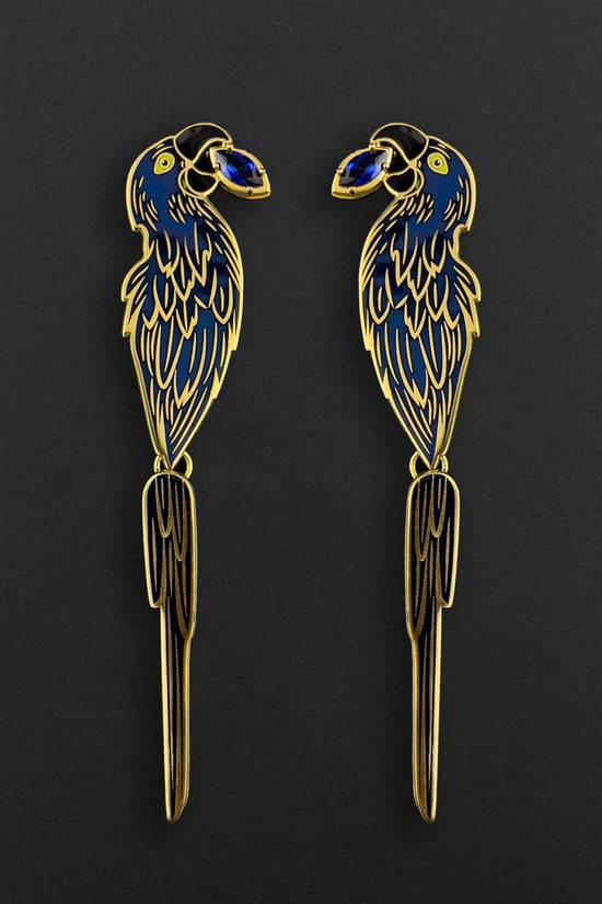 Two decorative macaw earrings with gold and blue details on a black background