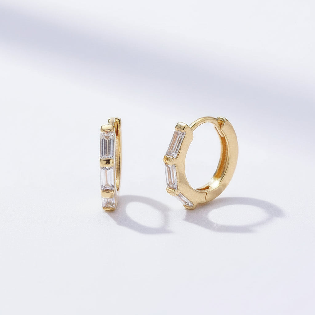 Gold hoop earrings with baguette cut stones on a light gray background