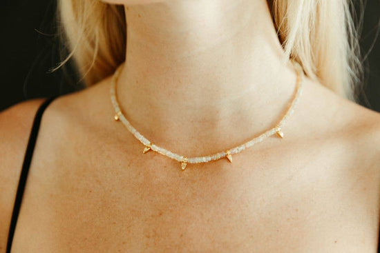Gold necklace with small triangular beads on a person's neck against a neutral background