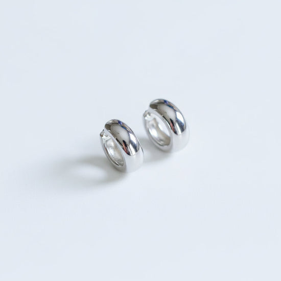 Pair of silver hoop earrings on a textured beige surface