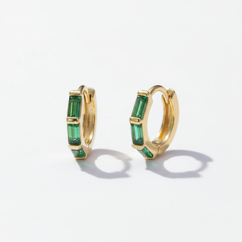 Gold hoop earrings with green gemstones on a light gray background