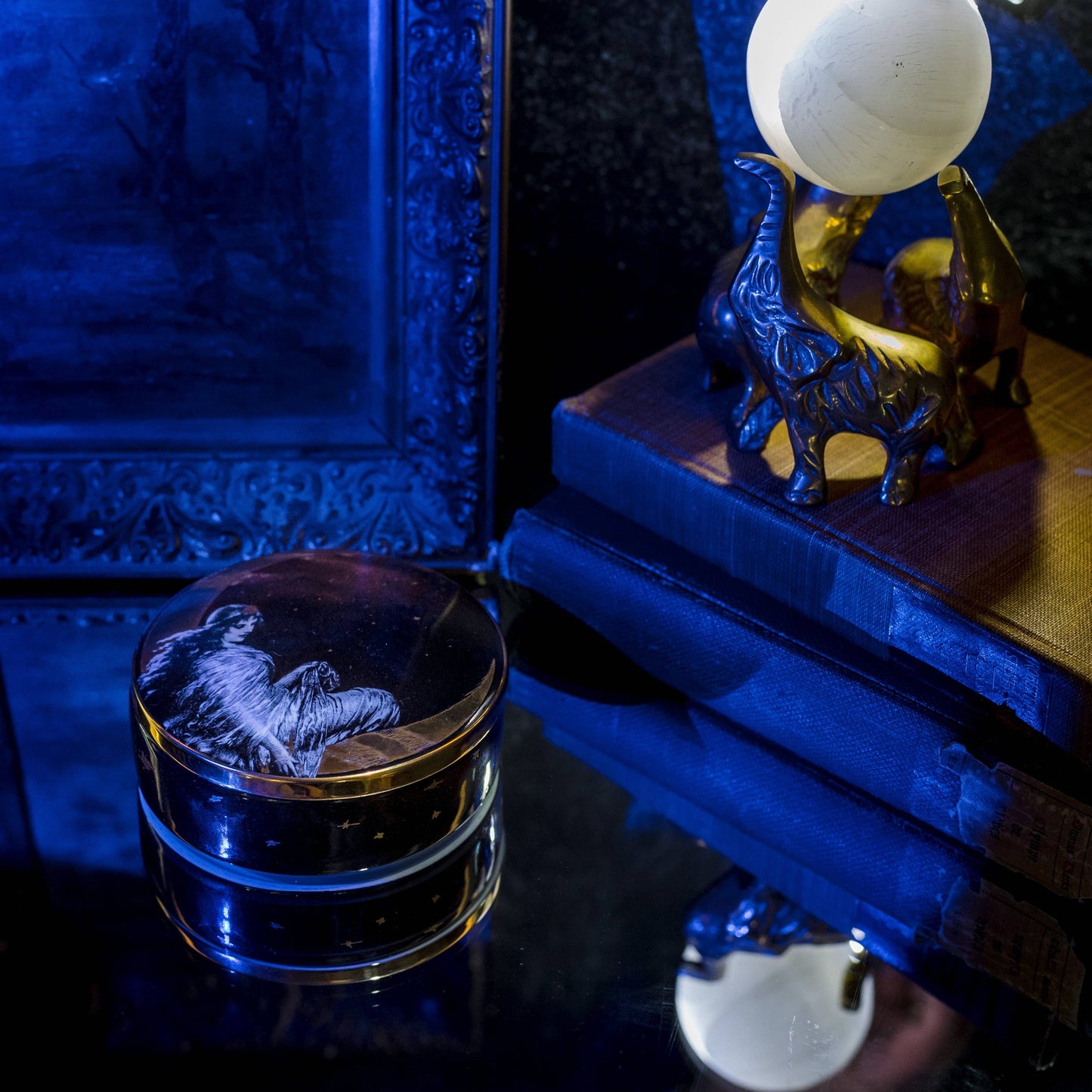 moon angel trinket box on a glass table with a crystal ball and stack of books in a blue light