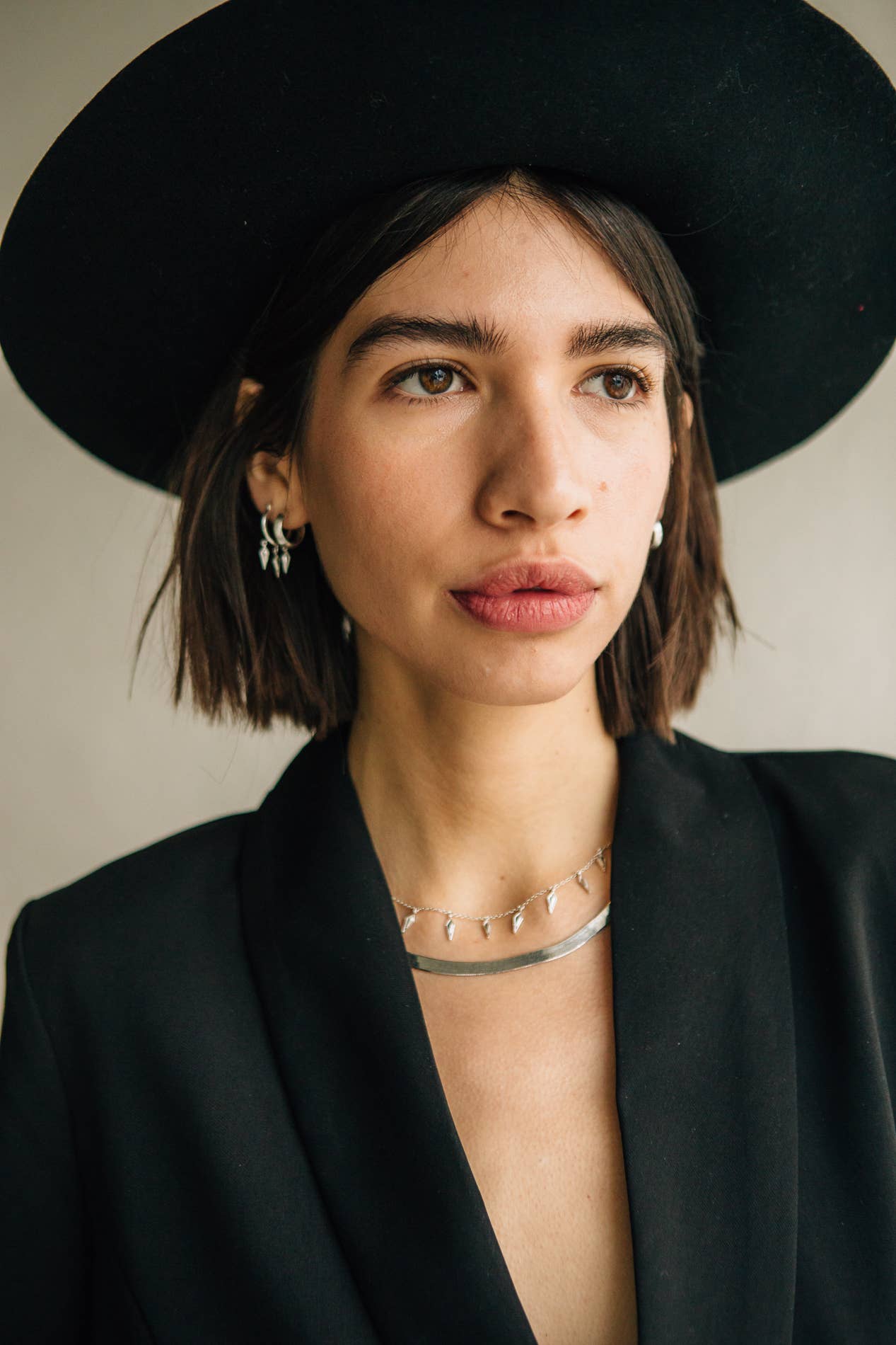 Woman wearing a black hat and black blazer with a neutral background