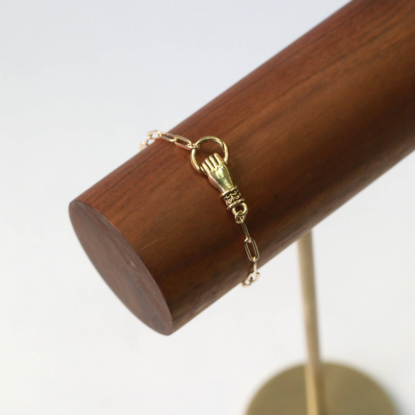Gold bracelet with a hand holding a circle on a wooden stand against a white background