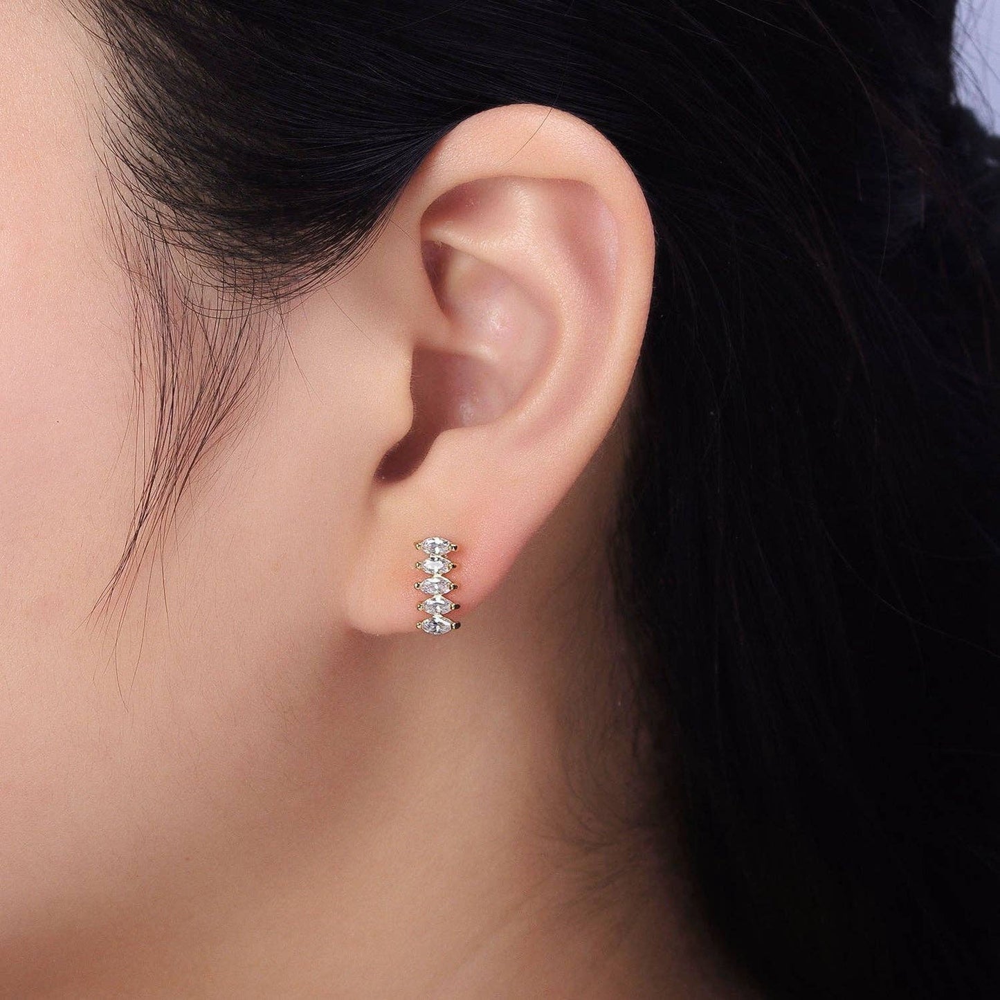 Close-up of an ear wearing a small silver earring with clear stones.