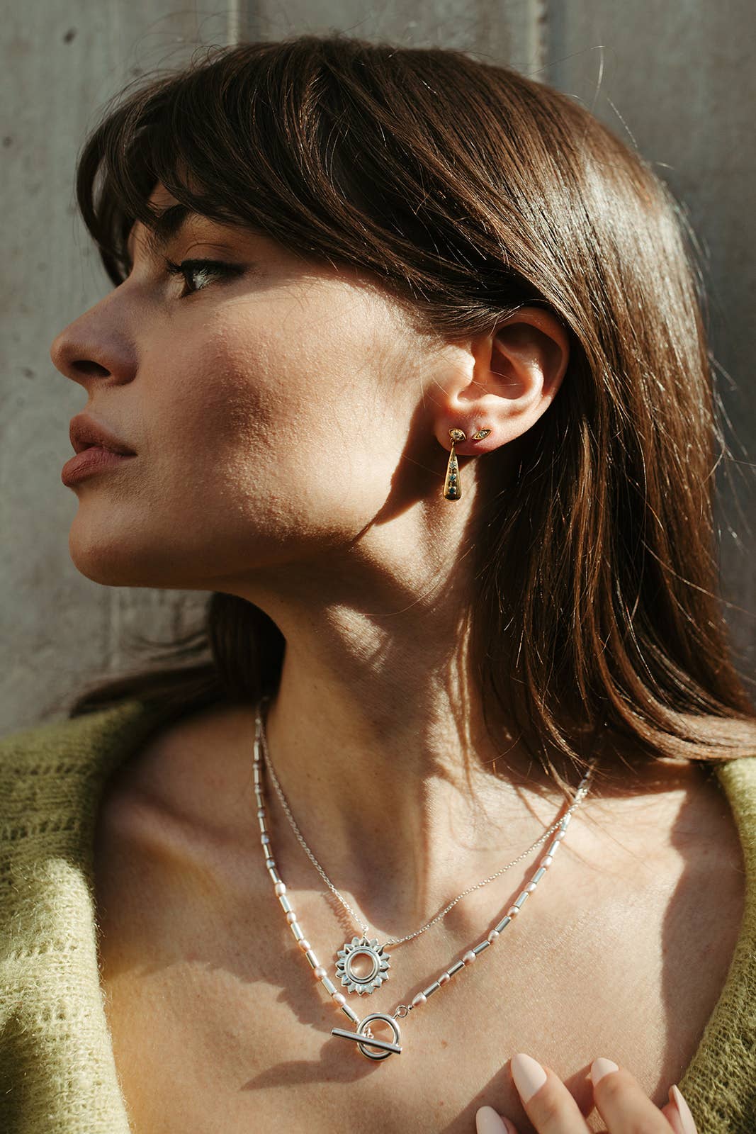 Woman wearing a silver necklace and earrings against a neutral background