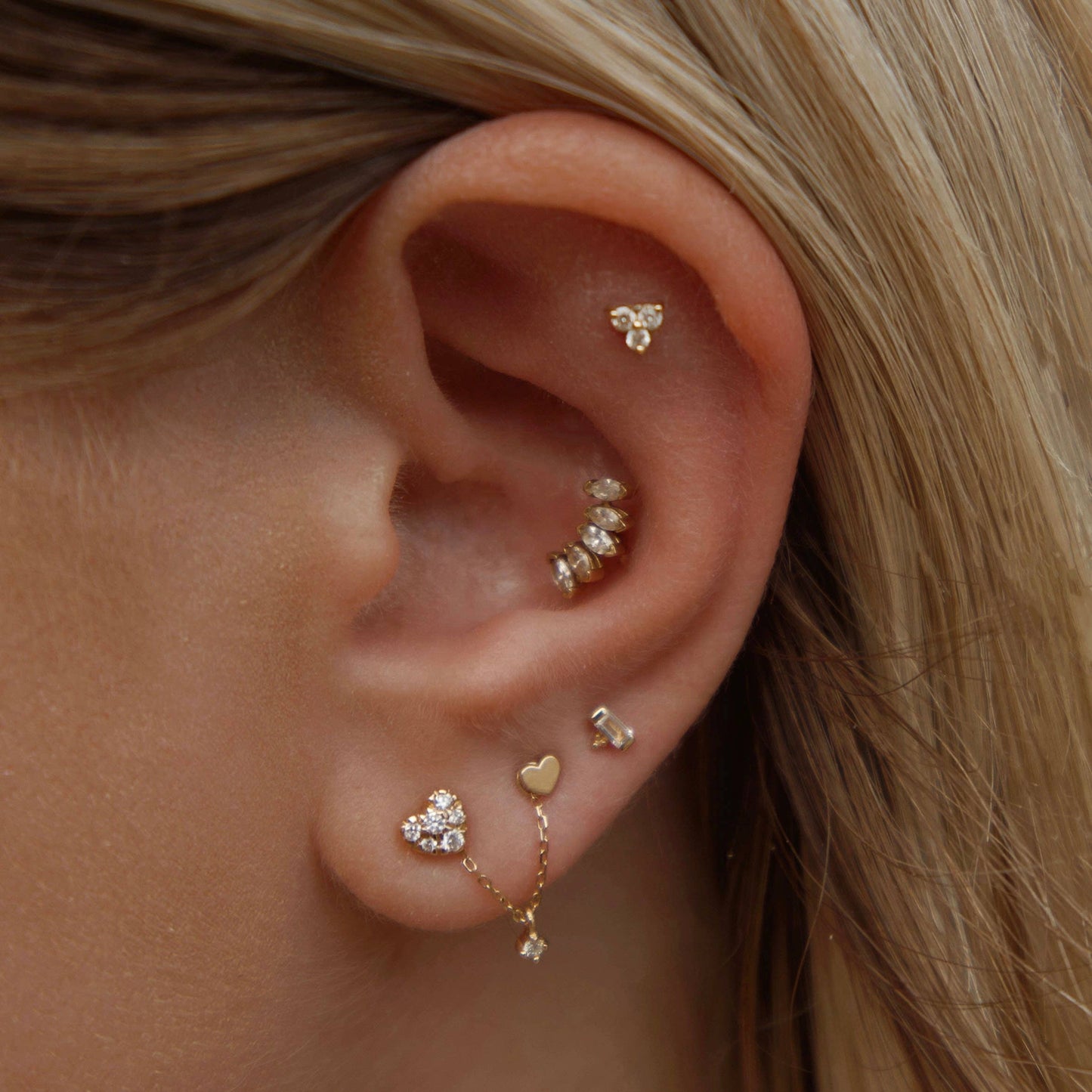 close up of a model wearing the 14k tiny dance piercing stud with 4 other gold and sparkly earrings on a white background