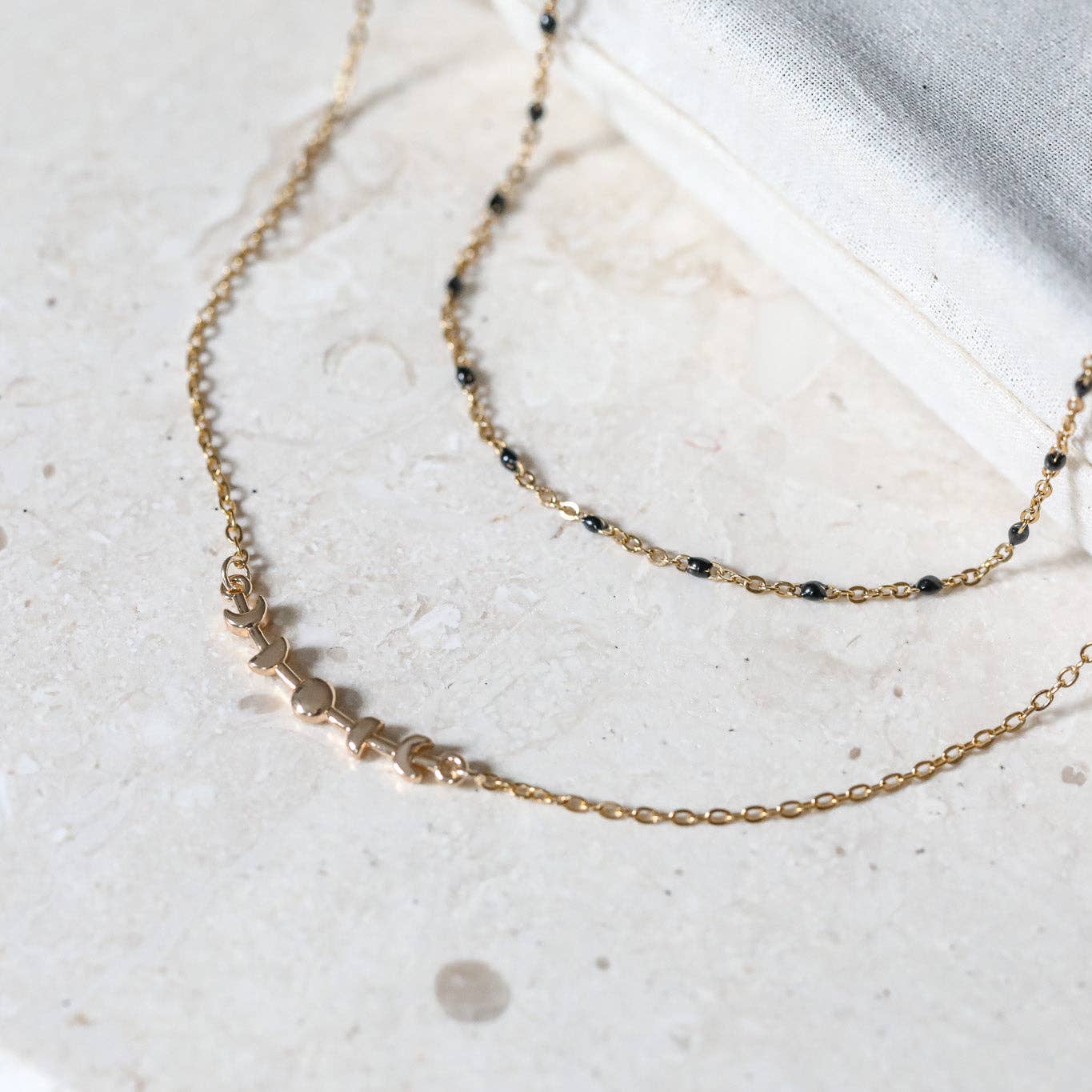 Two gold necklaces with small beads on a light stone surface