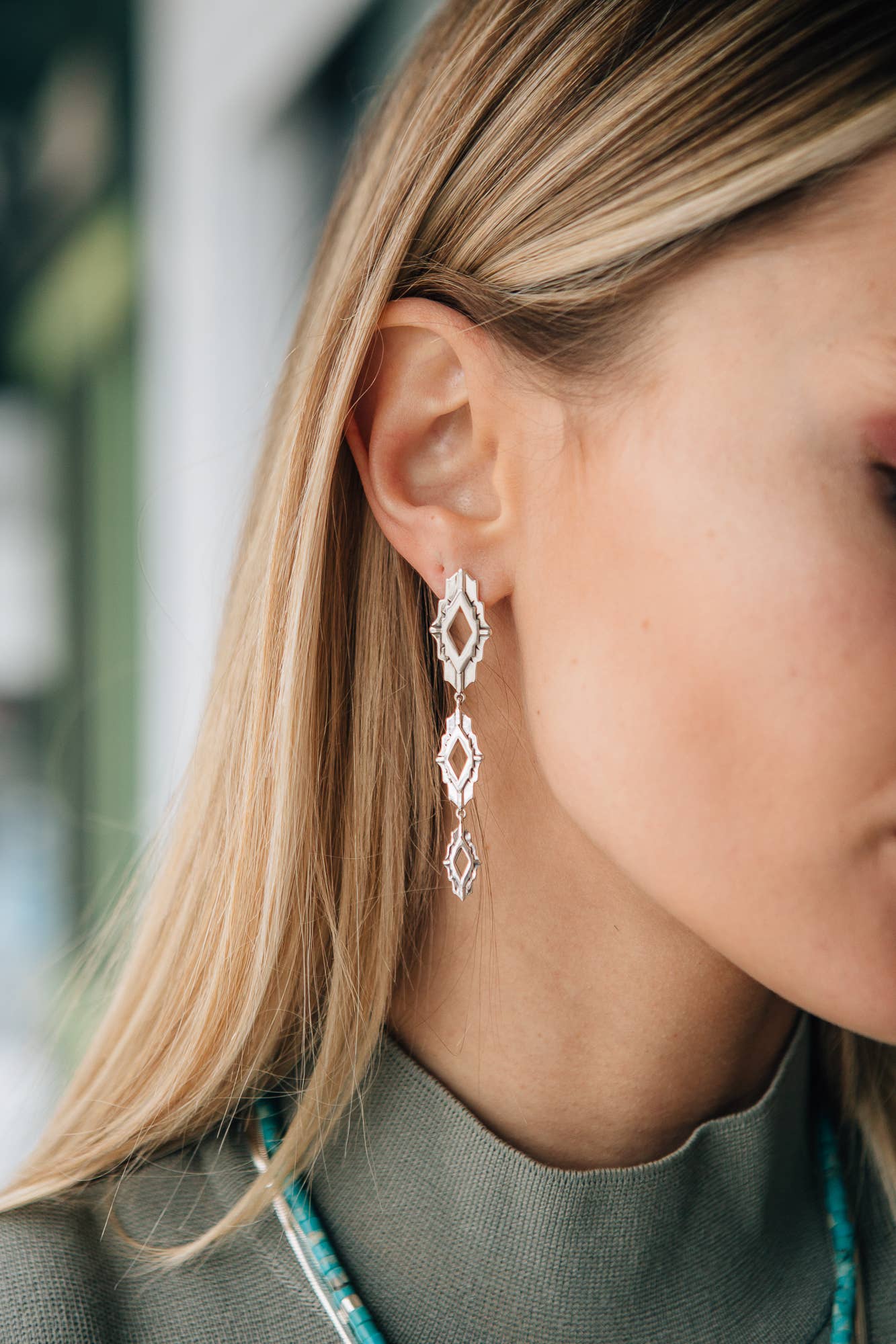 Close-up of a person wearing diamond-shaped earrings with a blurred background