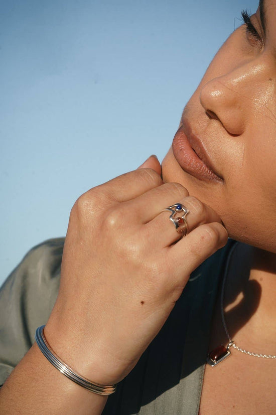 model wearing the kimbal cuff and two rings with their hand next to their face and a blue background