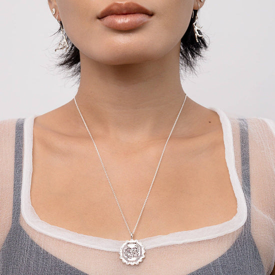 Close-up of a person wearing a silver necklace with a pendant on a plain background