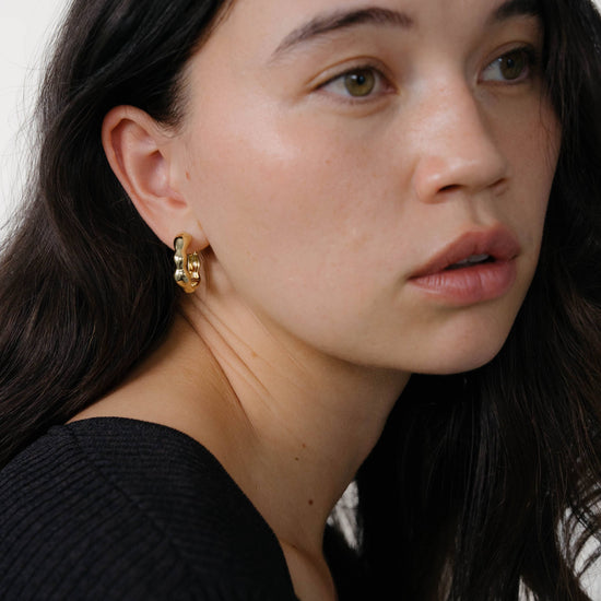 Woman wearing gold earrings with a neutral background