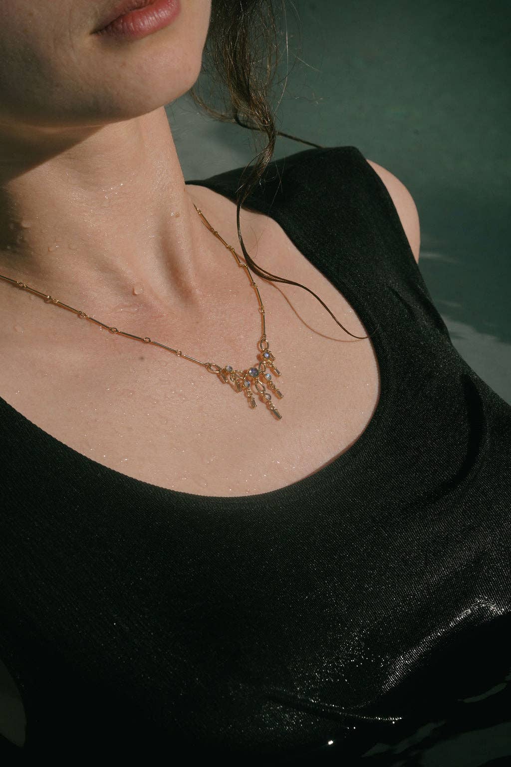 Close-up of a person wearing a black top and gold necklace with a green background