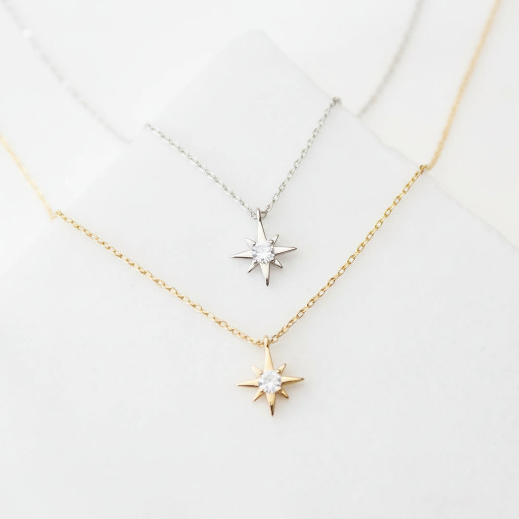 Two star-shaped pendants on gold necklaces against a light gray background