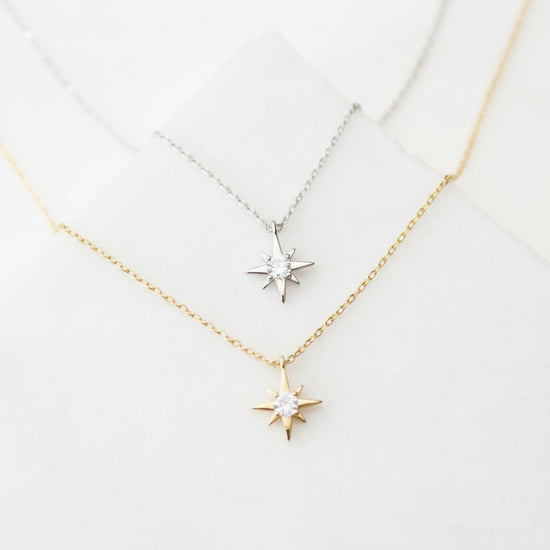 Two star-shaped pendants on gold necklaces against a light gray background