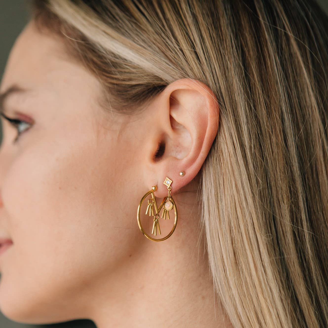 Close-up of a woman wearing gold hoop earrings with a small pendant.