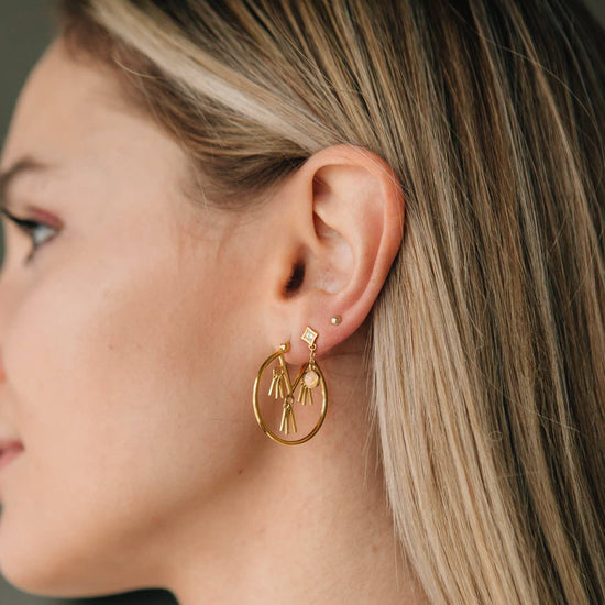 Close-up of a woman wearing gold hoop earrings with a small pendant.