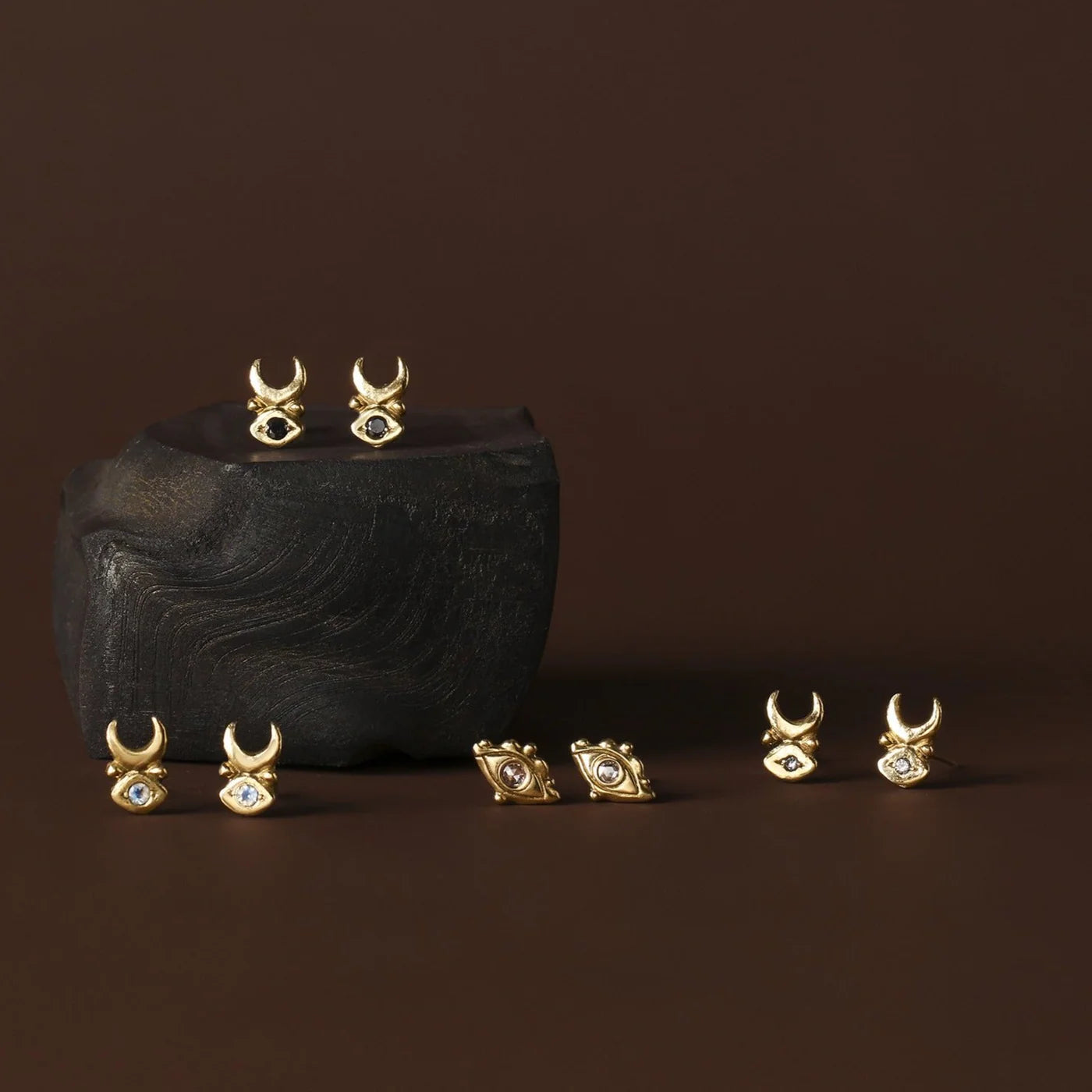 Gold earrings with gemstones on a dark stone surface against a brown background