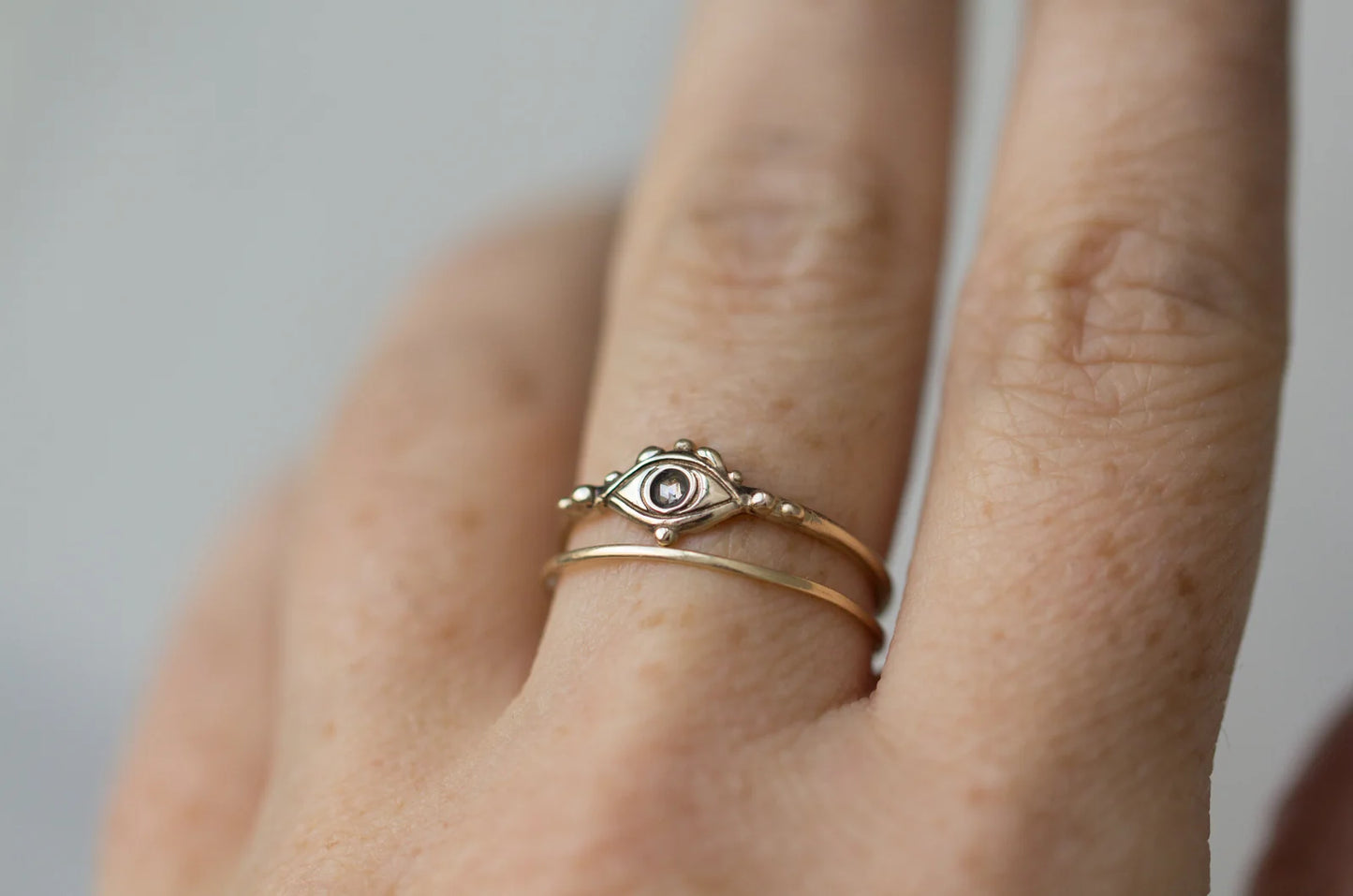 Close-up of a hand wearing two gold rings with a subtle design on a neutral background