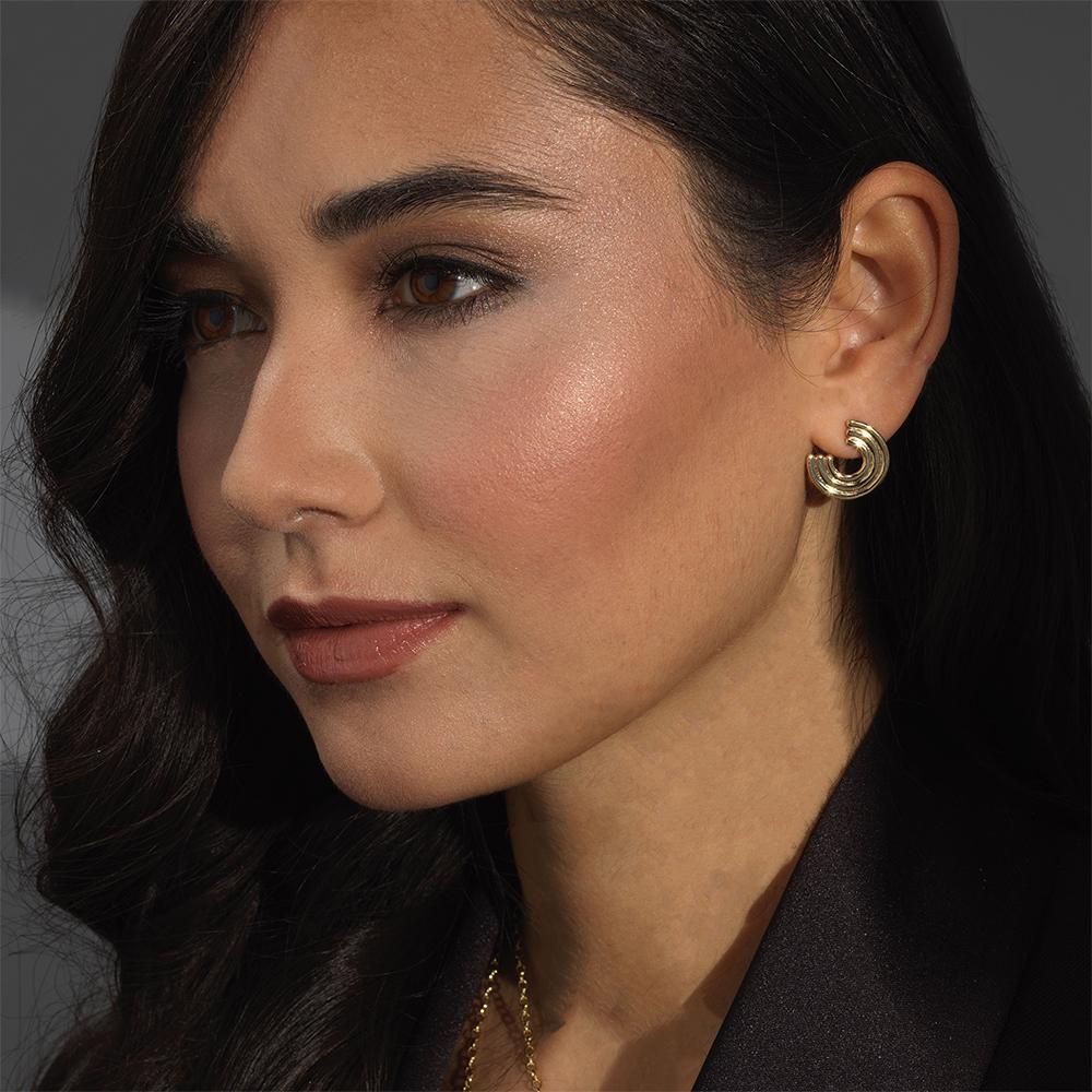 woman wearing gold stuff rainbow shaped earrings on grey background 