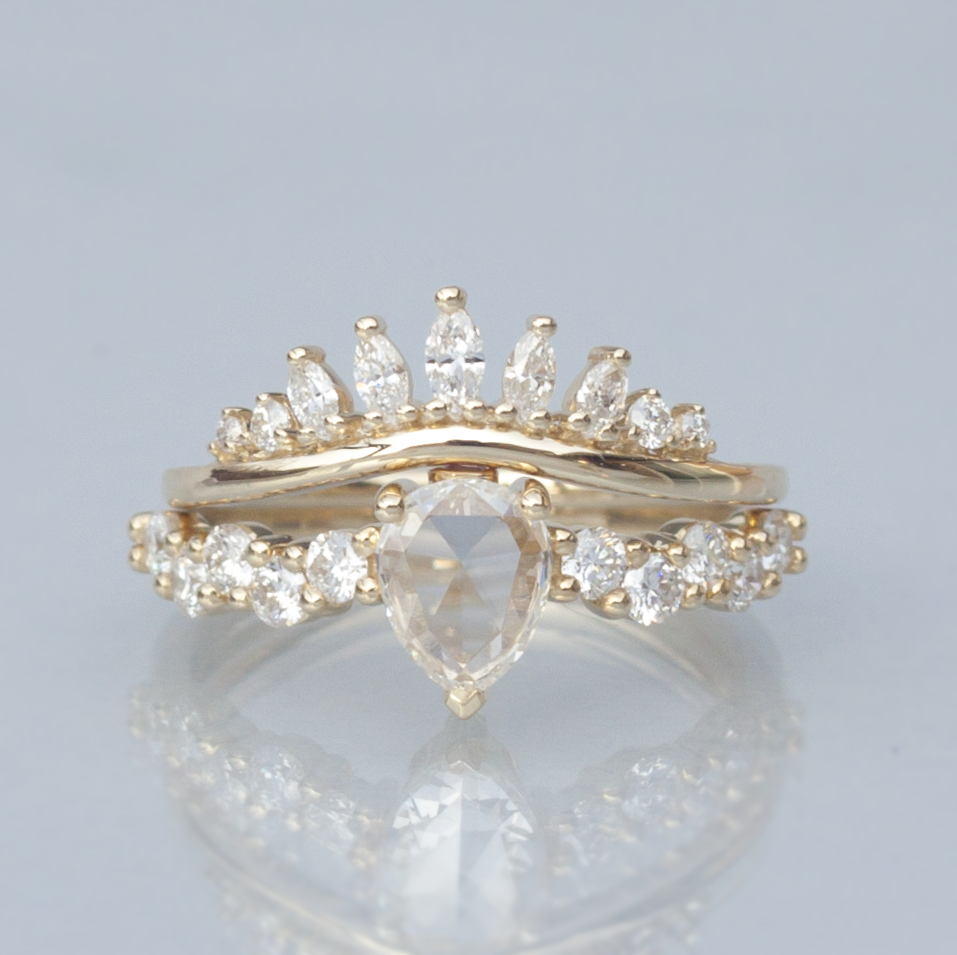 White diamond intertwine ring stacked with a diamond halo band, close up on light grey background.
