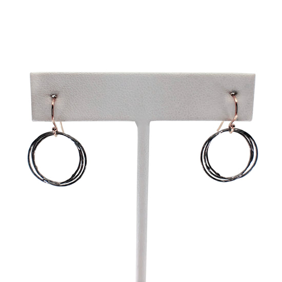 Oxidized silver and rose gold triple circle earrings on earring stand with white background.