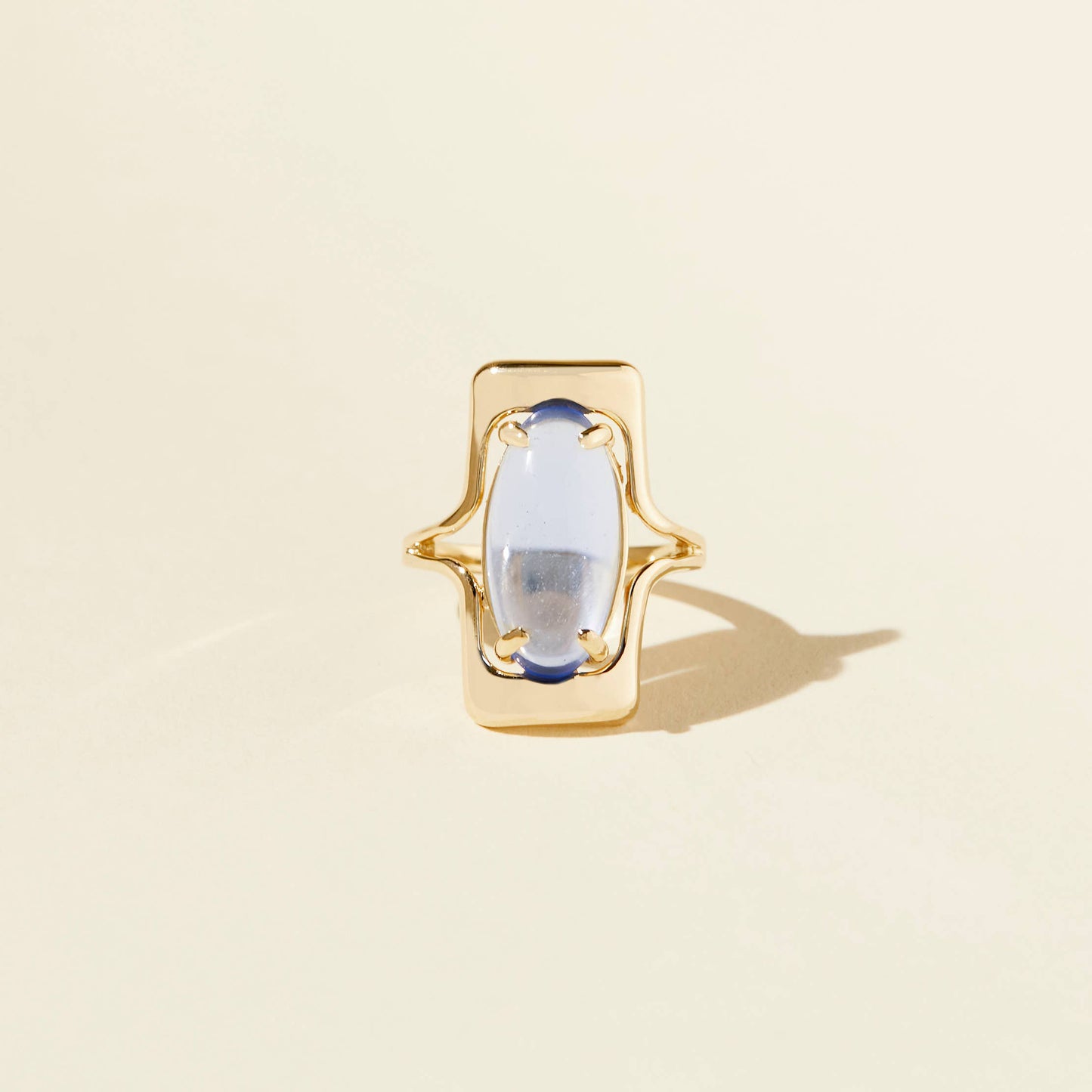 the blue walton ring with a large oval blue glass cabochon and curved gold accents on a beige background