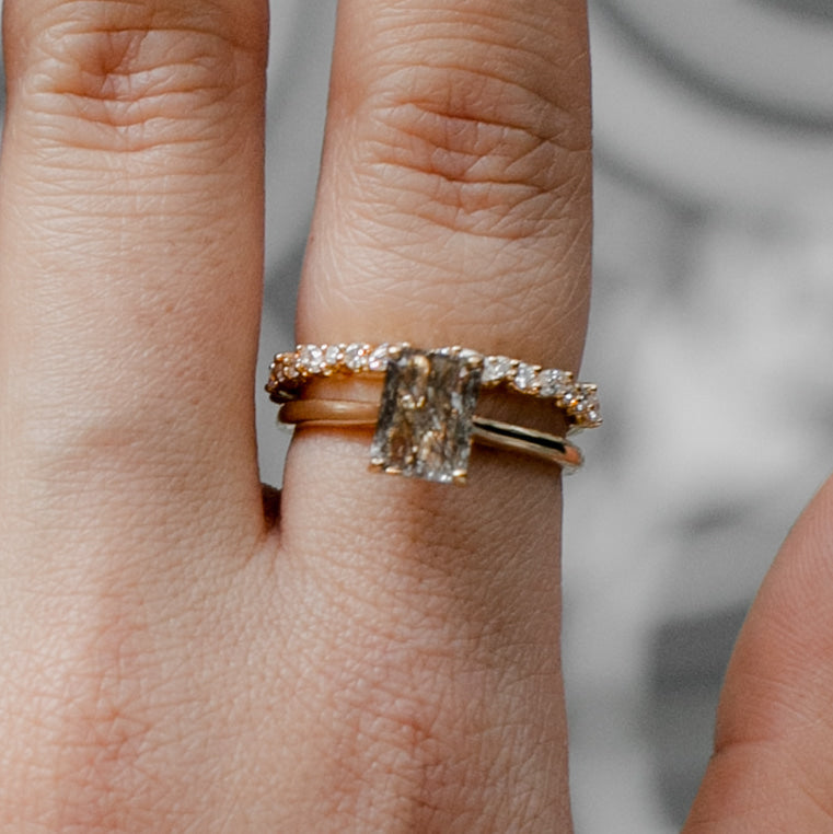 Single stone cut, gold ring alongside a diamond detailed ring on someones hand 