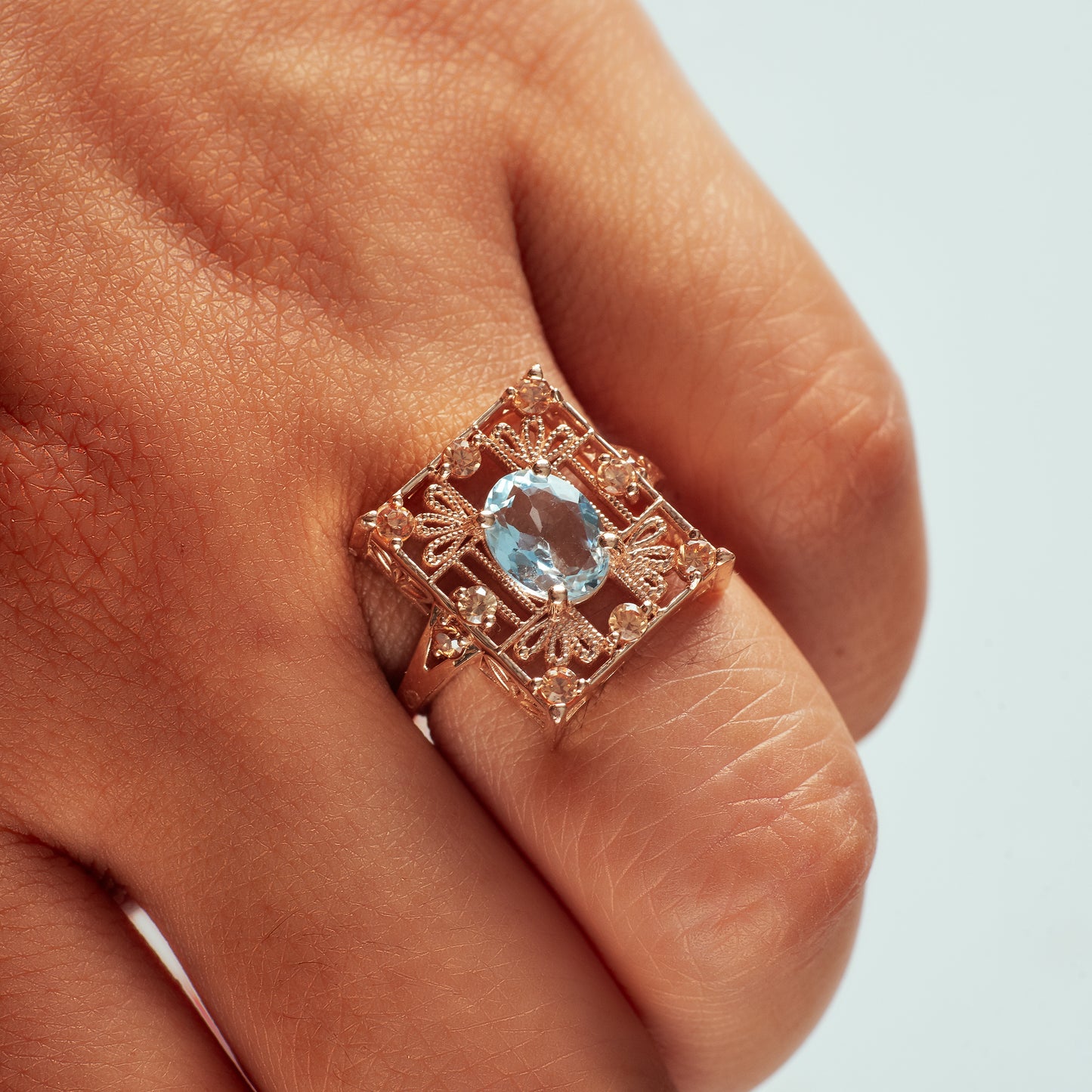14k rose gold rectangle shaped ring with detailed metalwork, champagne diamonds, and an aquamarine center stone modeled on hand.
