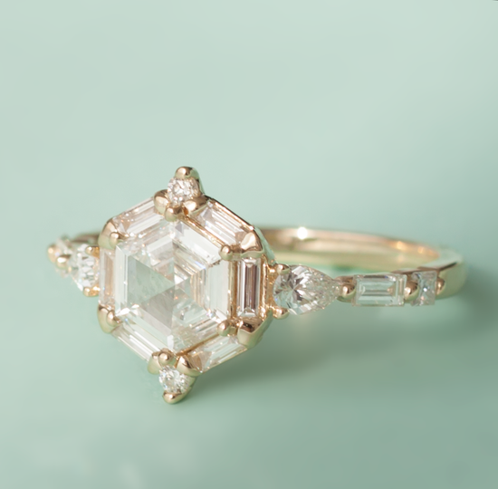 Diagonal view of the hexagon diamond ring with white diamond accents on band, close up on green background.