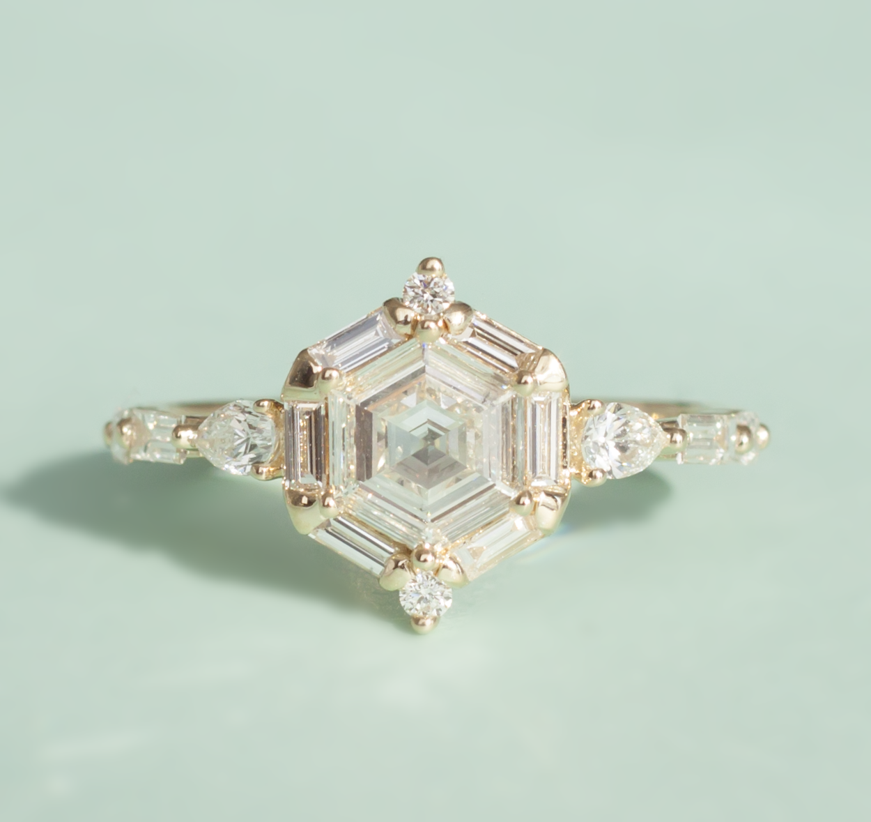 Hexagon diamond ring with white diamond accents on band, close up on green background.
