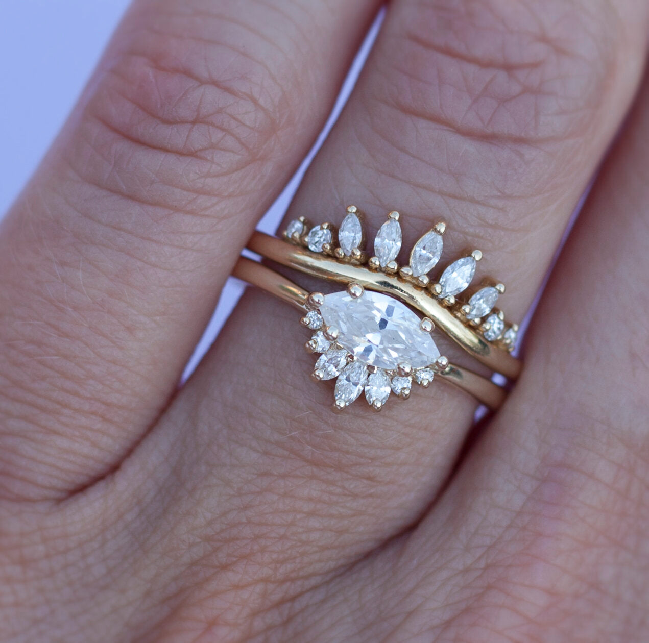 White diamond sideways set marquise gold ring with diamond crown, stacked with diamond band on a hand.