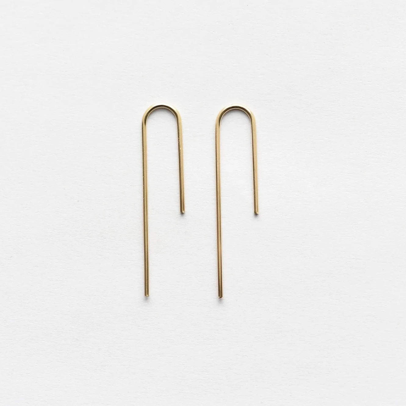gold asymmetrical arch threader earrings on white background